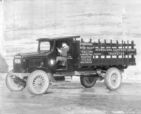 View of a man sitting in the driver's seat of an International delivery truck. The sign on the side of the truck reads: "International Harvester Company of America, Transfer, Albany, NY."