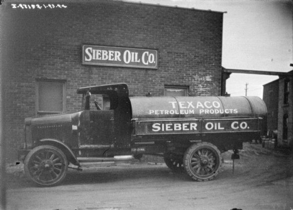 View of an oil delivery truck parked in front of a brick building with a sign for "Sieber Oil Co." The sign painted on the side of the truck reads: "Texaco Petroleum Products, Sieber Oil Co."