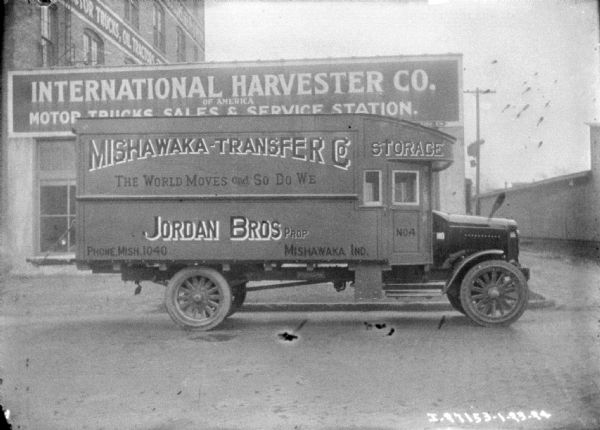 Delivery truck parked in front of an International Harvester Company of America motor trucks, sales, and service building. The sign painted on the side of the truck reads: "Mishawaka-Transfer Co."