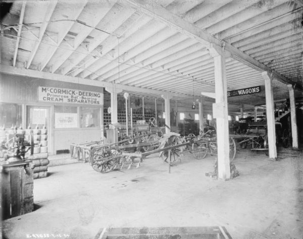 Interior view of a dealership. A sign on the wall reads: "McCormick-Deering Primrose Ball-Bearing Cream Separators." Merchandise on display includes a tractor, cream separators and wagons.