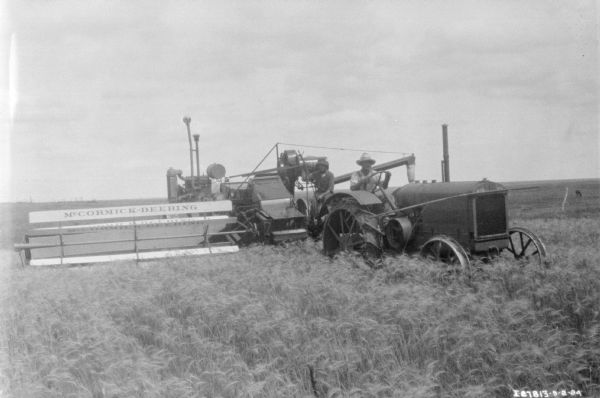 Three-quarter view from front of two men on a tractor pulling a binder in a field.