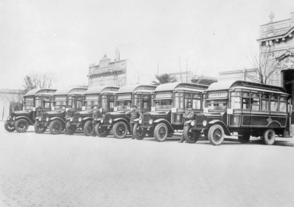 Men standing with a fleet of buses. The sign on each bus reads: "Chacarita."