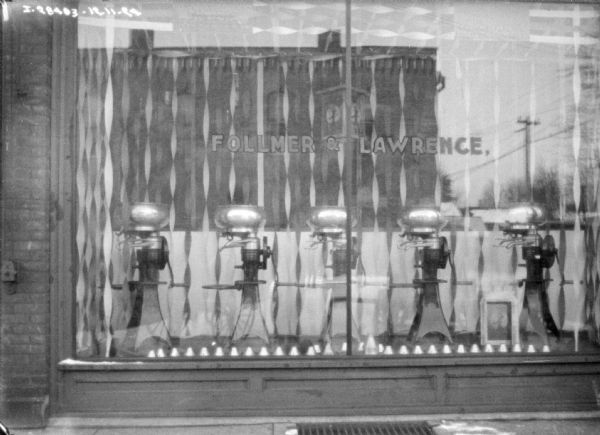 Exterior view of a display of cream separators on display in a show window. The sign on the window reads: "Follmer & Lawrence."