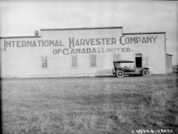 View across field towards a Model T parked in front of a dealership. The large sign painted on the side of the building reads: "International Harvester Company of Canada, Limited."