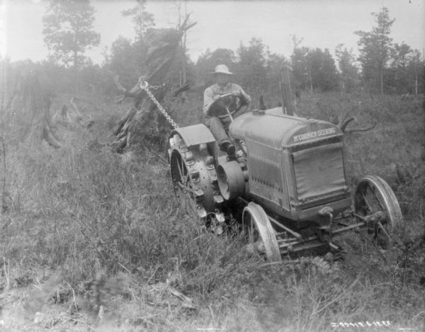 Three-quarter view from front right of a man using a tractor to pull stumps in a field.