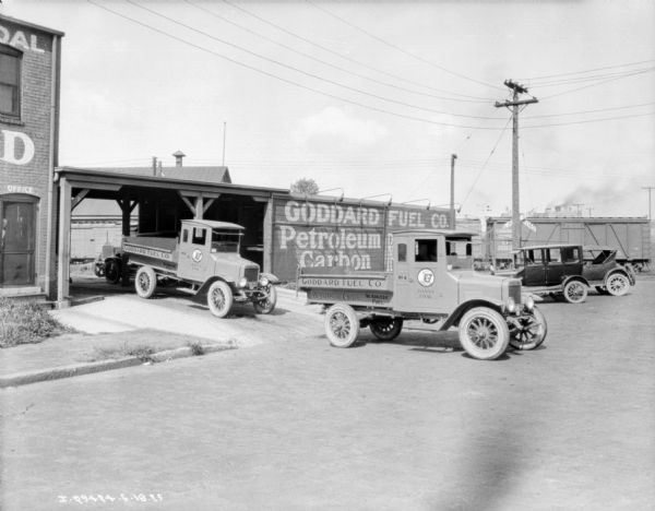 View from street towards delivery trucks leaving the Goddard Fuel Co. In the background is a train and a railroad crossing.