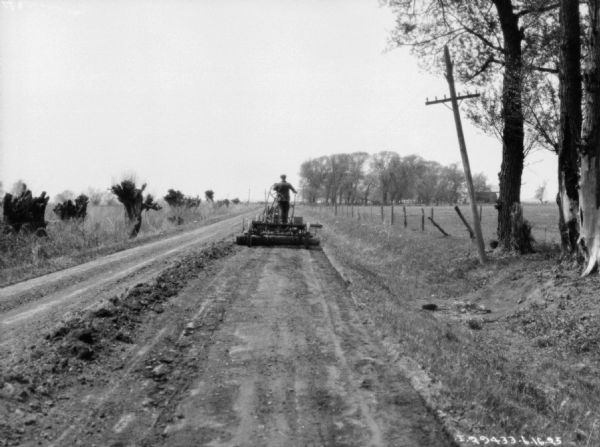 Rear view down road towards a man on a tractor pulling a road leveler.