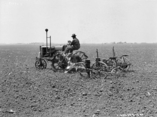Left side view of a man driving a Farmall tractor pulling a planter in a field.