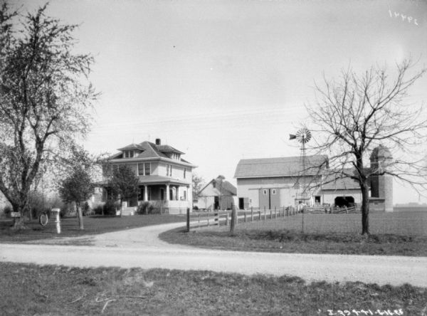 View across road towards a farm with windmill and silo. There is a tire swing in the front yard on the left.