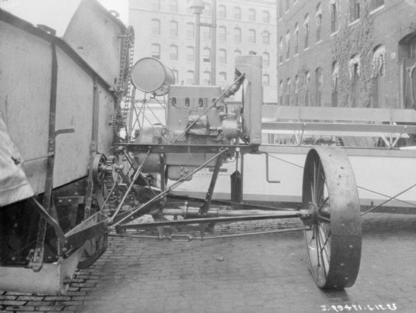 Close-up of the side of a harvester thresher parked on cobblestones outdoors near a large brick building.