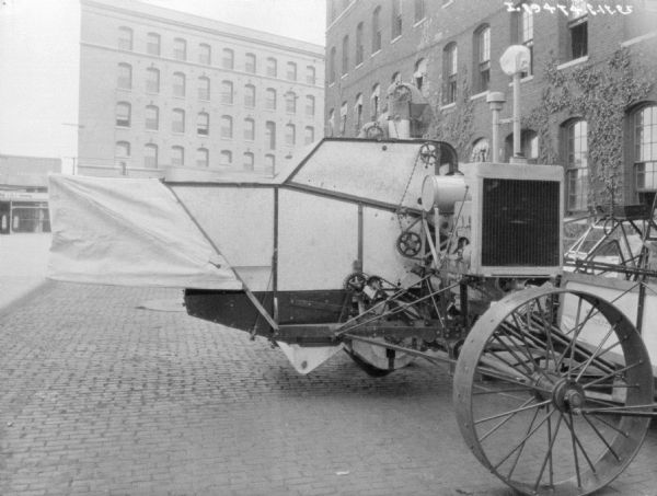 Harvester thresher parked on cobblestones outdoors near large brick buildings.