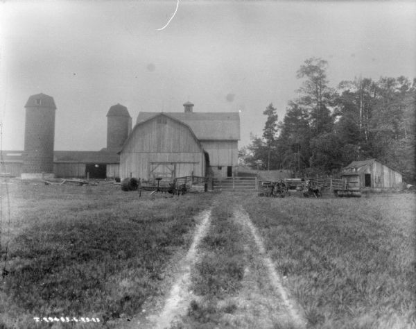 View down two-track path in a field towards farm implements and farm buildings.