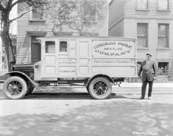 View across street towards a man standing near a Chicago Pure Milk Company delivery truck parked on the opposite curb. 