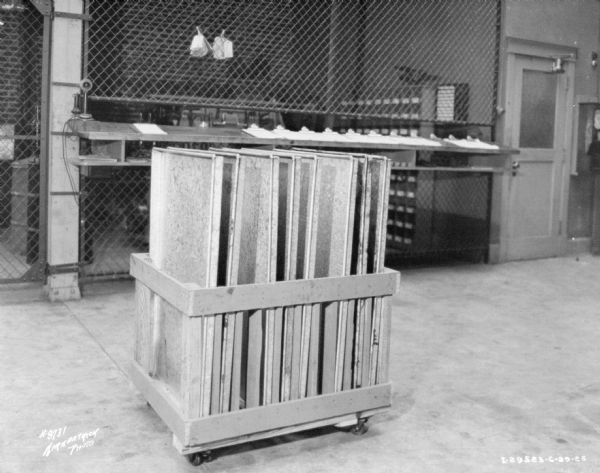 Interior view of a repair shop. In the foreground is a cart loaded with material. In the background is a wall made of wire fencing that separates the shop from another room. 