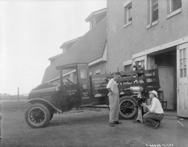 A salesman with a McCormick-Deering truck is showing a farmer a cream separator. There is a large barn behind the truck.