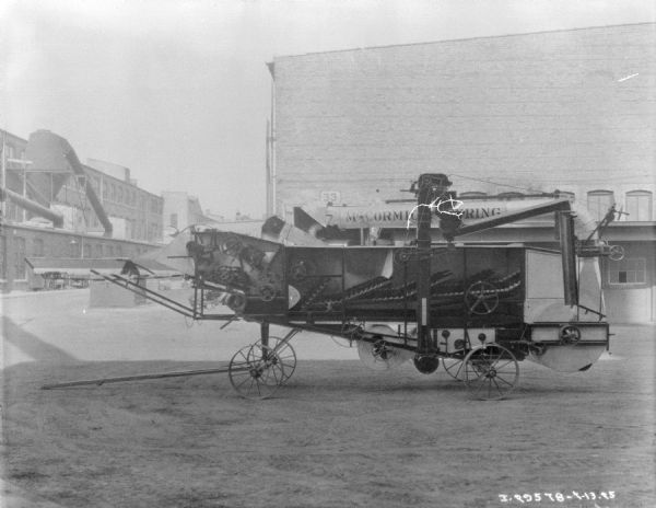 McCormick-Deering harvester thresher parked outdoors. There are factory buildings in the background.