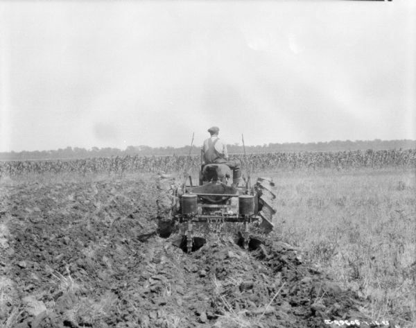 Rear view of a man driving a Farmall tractor planting in a field.