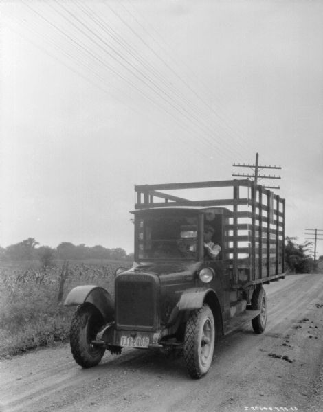 Three-quarter view from front left of a man driving a farm truck with a stake body. The truck has an Indiana license plate.
