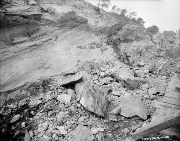 View of rubble along an exposed rock face. Construction equipment is in the far distance.