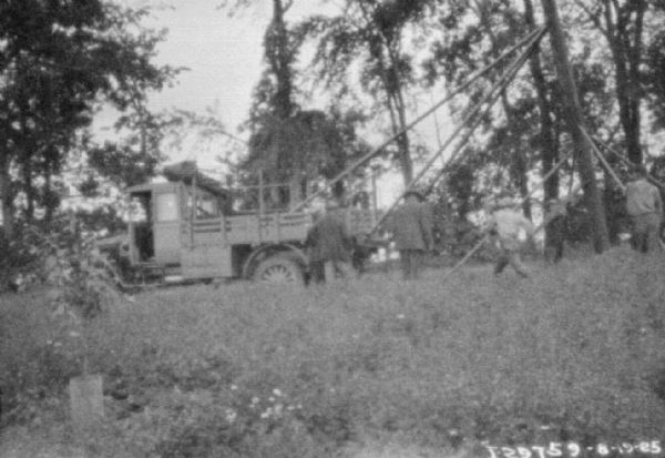 A group of men are standing near a truck being used for tree removal.
