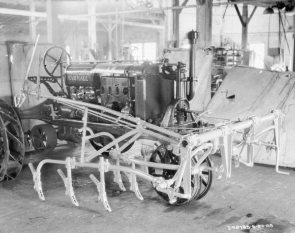 View of a cultivator on a Farmall tractor on what may be a factory floor.