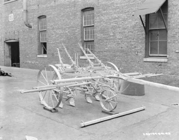 A two row cultivator displayed on the pavement in front of a brick factory building.
