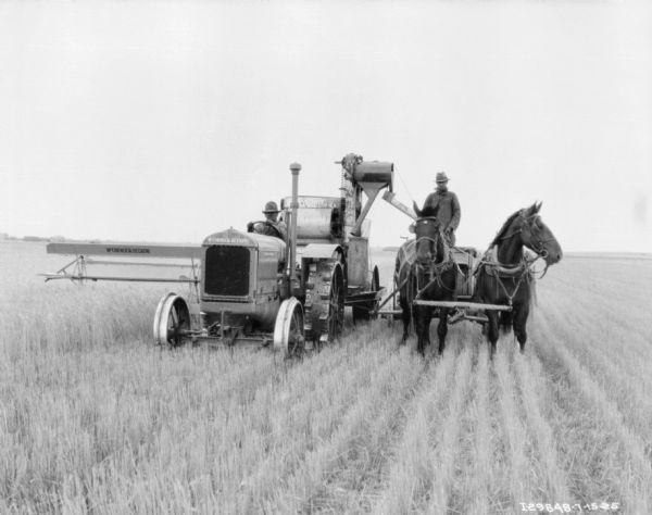 View from front of a man on a McCormick-Deering tractor pulling a McCormick-Deering No. 8 power drive harvester thresher in a field. Alongside on the right is a man on a horse-drawn wagon drawn by two horses wearing fly-nets.
