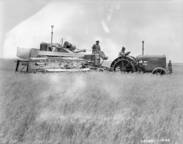 Right side view of a man driving a tractor to pull a McCormick-Deering No. 8 power drive harvester thresher.