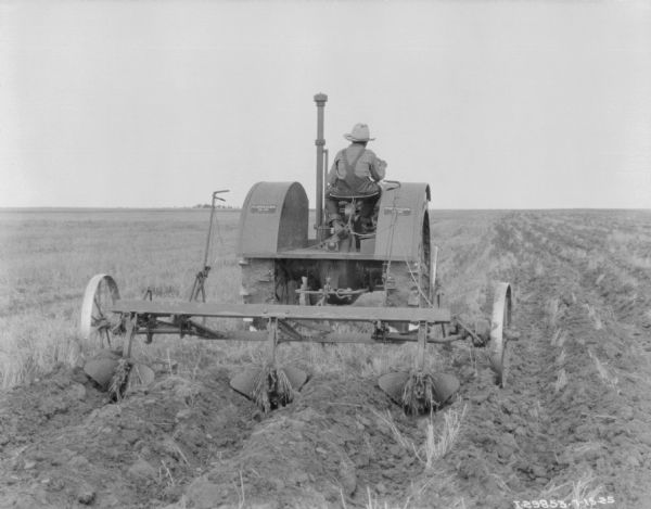 Rear view of a young boy driving a McCormick-Deering 15-30 tractor pulling a cultivator in a field.
