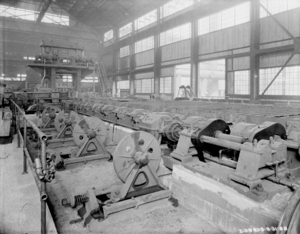 Power generators inside a factory. The ceiling is exposed, and rows of windows are letting in natural light.