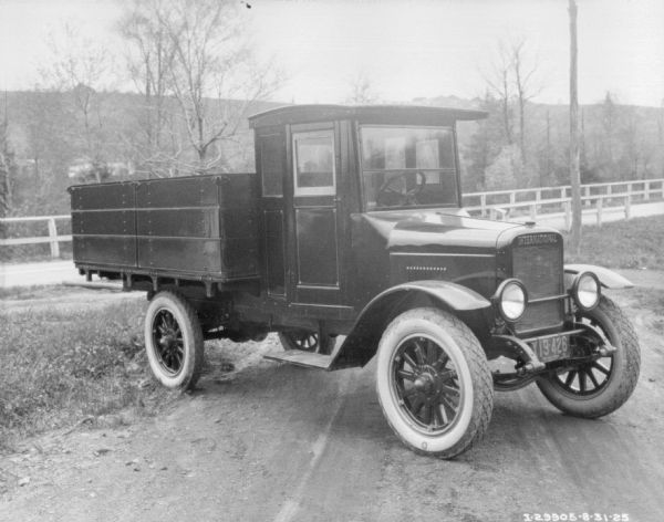 Three-quarter view from front right of a truck. The truck is parked at an angle on the side of a fence-lined road. A hill or mountains are in the background.