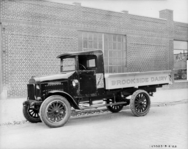 View across street towards a delivery truck parked near the curb. In the background is a brick, one-story building. The signs painted on the side of the truck read: "George Schlicht," and "Brookside Dairy."