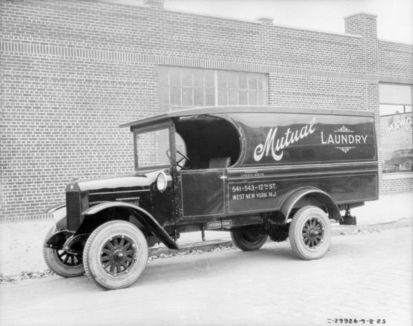 View across street towards a delivery truck for Mutual Laundry parked near the curb. In the background is a brick, one-story building. The sign painted on the side of the truck read: "West New York N.J."