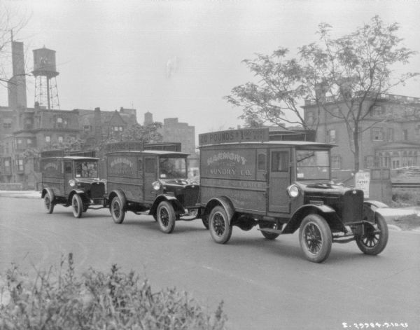 Three delivery trucks in a row on a street. There are buildings and a water tower in the background.