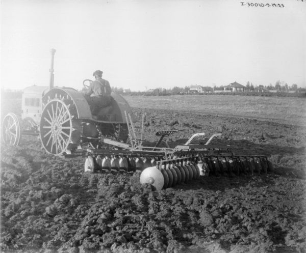 Rear view of a man driving a tractor disking a field.