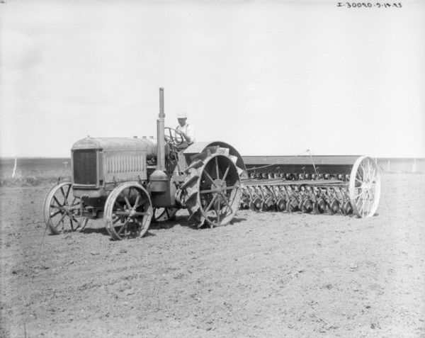 Three-quarter view from front left of a man on a McCormick-Deering tractor seeding a field.