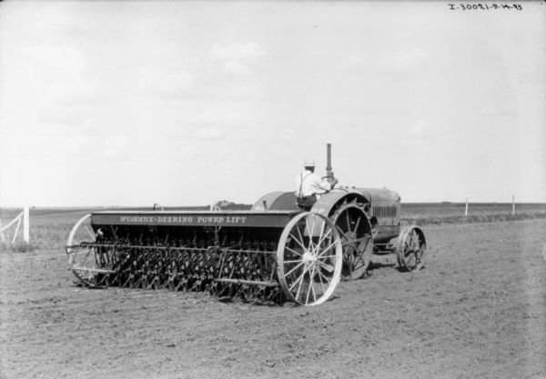 Three-quarter view from right rear of a man driving a 15-30 HP tractor to seed a field.