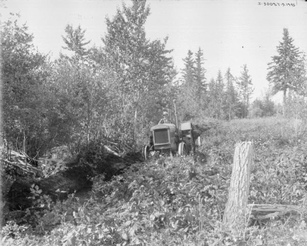 A man is driving a McCormick-Deering tractor to clear a field near a forest.