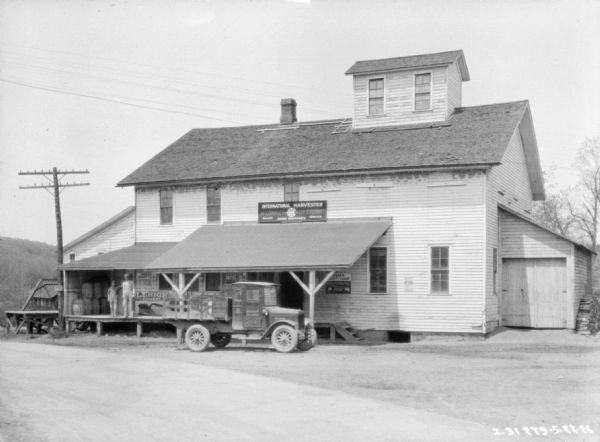 View across road towards a dealership. There is a truck parked near a loading dock. There are two men standing on the loading dock.