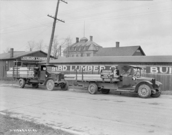 View across road towards two lumber delivery trucks parked in front of the Howard Lumber Co.