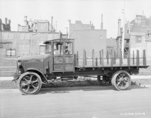 View across street towards a delivery truck parked alongside a curb. Painted on the side of the truck is a sign that reads: "The Peoples Gas Light & Coke Co." 