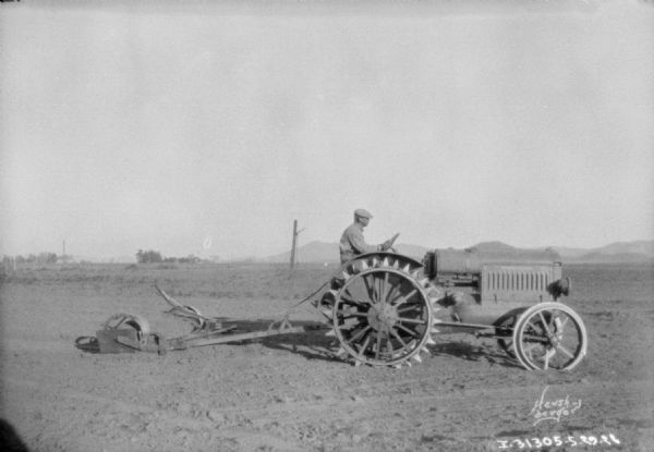 Right side view of a man driving a tractor pulling an agricultural implement in a field.