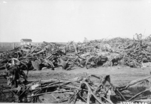View of a junkyard, of what appears to be made up of old agricultural equipment. There is a building in the far background.