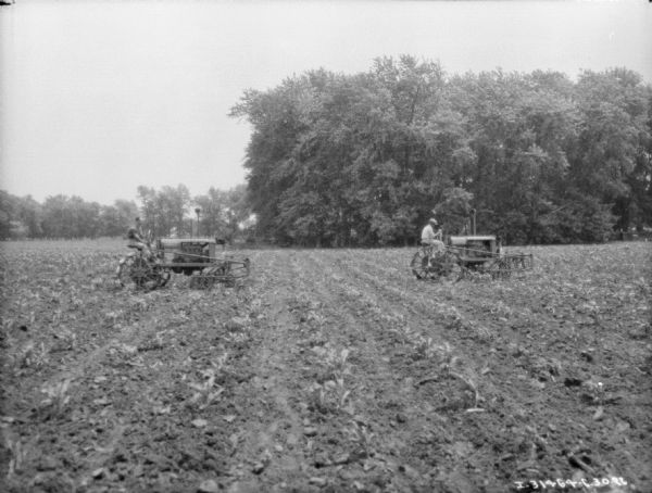 View across field towards two men with Farmall tractors working in a field.