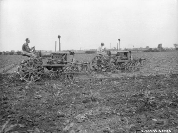 View across field towards two men with Farmall tractors working in a field.
