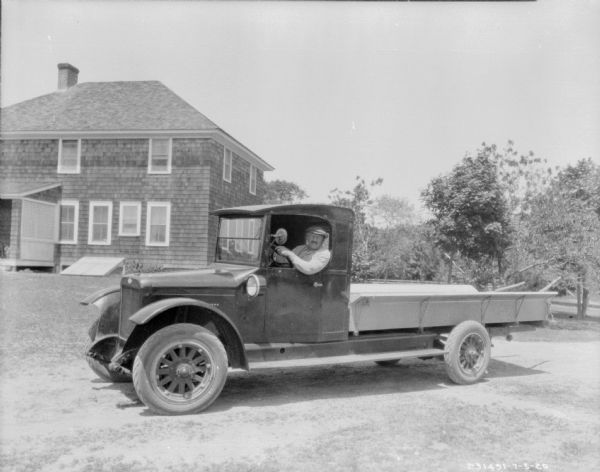 A man is sitting in the driver's seat of a truck parked in the front yard of a house.