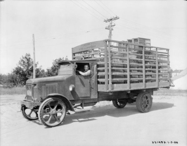 View towards a man sitting in the driver's seat of a delivery truck. A sign on the truck reads: "J.H. Gates Motor Transportation."