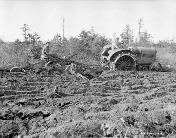 View of a man sitting a disk plow being pulled by a man on a 15-30 tractor in an overgrown area.