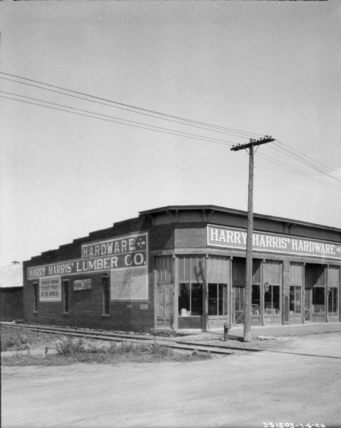 View from street towards the front and left side of the Harry Harris hardware store. There are railroad tracks in the foreground.