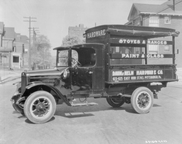 View of a delivery truck parked in the middle of a street. Signs on the side of the truck read: "Hardware," "Stoves & Ranges," "Paint & Glass," and "Daum & Helm Hardware Co."